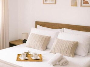 Ein ordentlich gemachtes Bett mit weißer Bettwäsche, einem Holzkopfschild und einem Tablett mit Tassen und einem Glas.