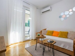 Ein modernes Wohnzimmer mit einer Couch, einem kleinen Tisch und einer Glastür zum Außenbereich.
