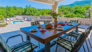 A covered outdoor dining area with a pool, stone walls, and a view of green hills. - Villa with swimming pool (Vrgorac)