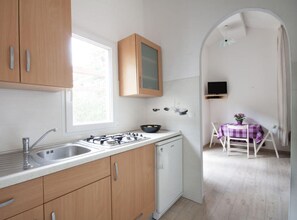 Eine Küche mit Holdekor, einem Gasherd, einer Spüle und einem Geschirrspüler. Über der Spüle befindet sich ein Fenster, und im angrenzenden Raum steht ein Tisch mit lila Tischdecke.