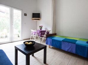 Ein Zimmer mit einem Bett, einem Tisch mit Obstschale, einem an der Wand befestigten Fernseher und einem Sessel mit Tisch.