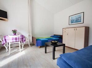 Ein kleiner, gut beleuchteter Raum mit einem Bett, einem Tisch mit einer Schale, einem Stuhl, einer Couch und einem Schrank.