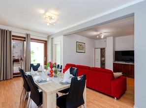 Ein Essbereich mit einem Holztisch, gedeckt für vier Personen, einem roten Sofa, einer Küchenzeile mit Schränken und einem Fernseher.