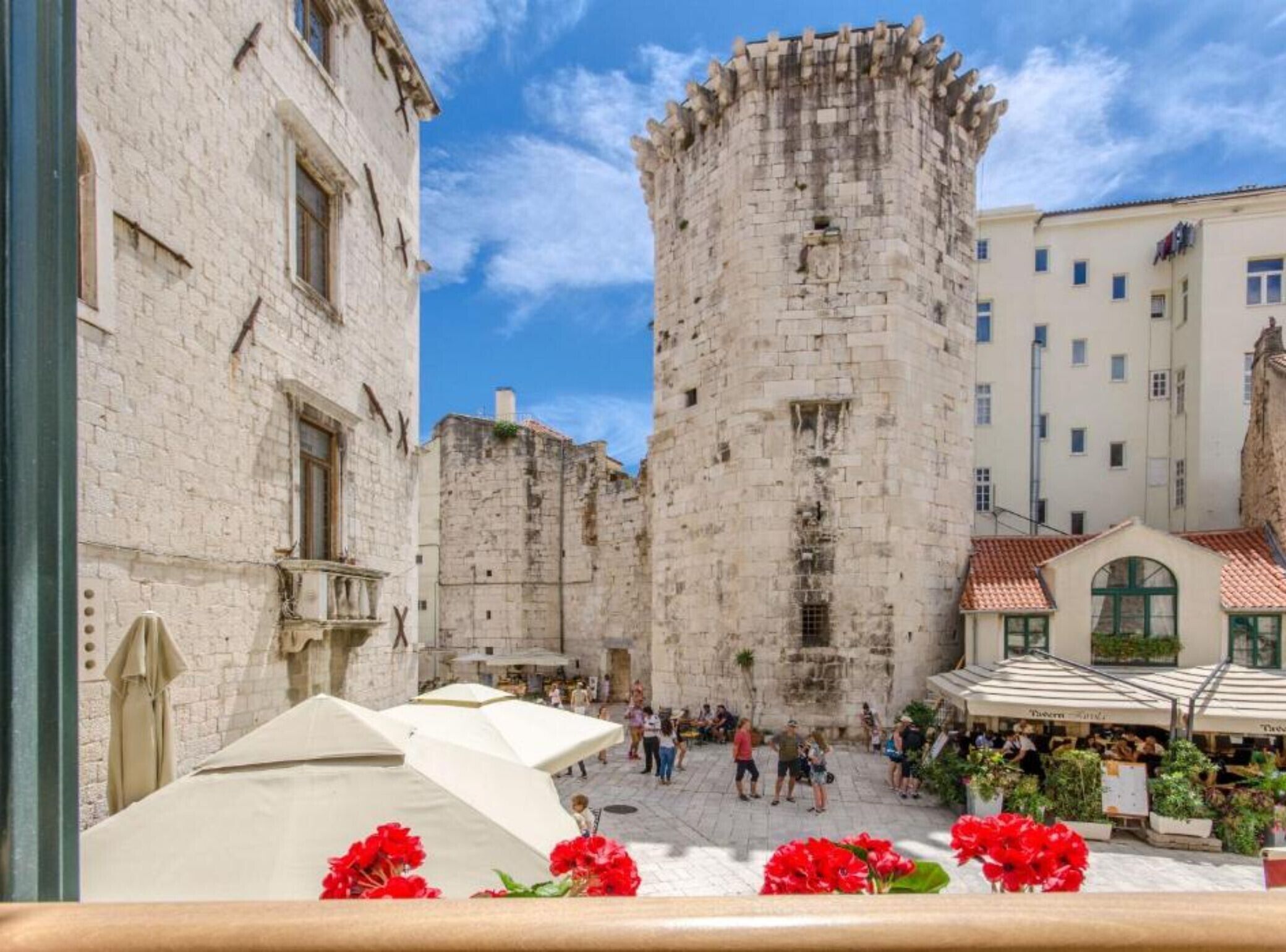 Ein historischer Steinturm mit Innenhof, umgeben von Gebäuden mit Balkonen und Außenbereichen zum Sitzen.
