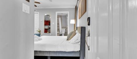 A narrow hallway leading to a bedroom with a bed, a bedside table, and a mirror.