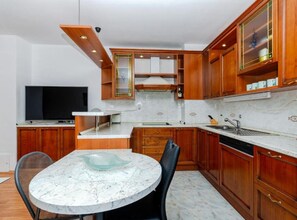 A compact kitchen with wooden cabinets, a marble countertop, and a dining table with chairs. - Comfort Three Bedroom Apartment with Terrace and Sea VIew (Split)