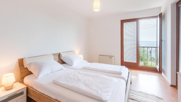 Une chambre avec deux lits, une table de chevet avec une lampe, un radiateur et une vue sur l’extérieur grâce à une porte coulissante.