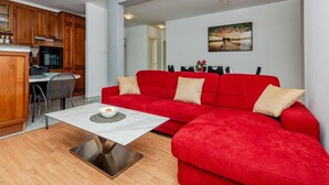 Un salon moderne avec un canapé rouge, une table basse blanche et un coin cuisine doté de meubles en bois.