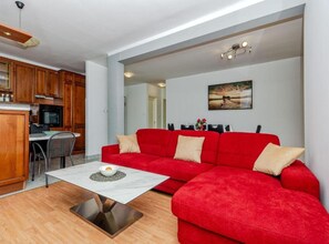 A modern living room with a red sofa, a white coffee table, and a kitchen area with wooden cabinets. - Comfort Three Bedroom Apartment with Terrace and Sea VIew (Split)