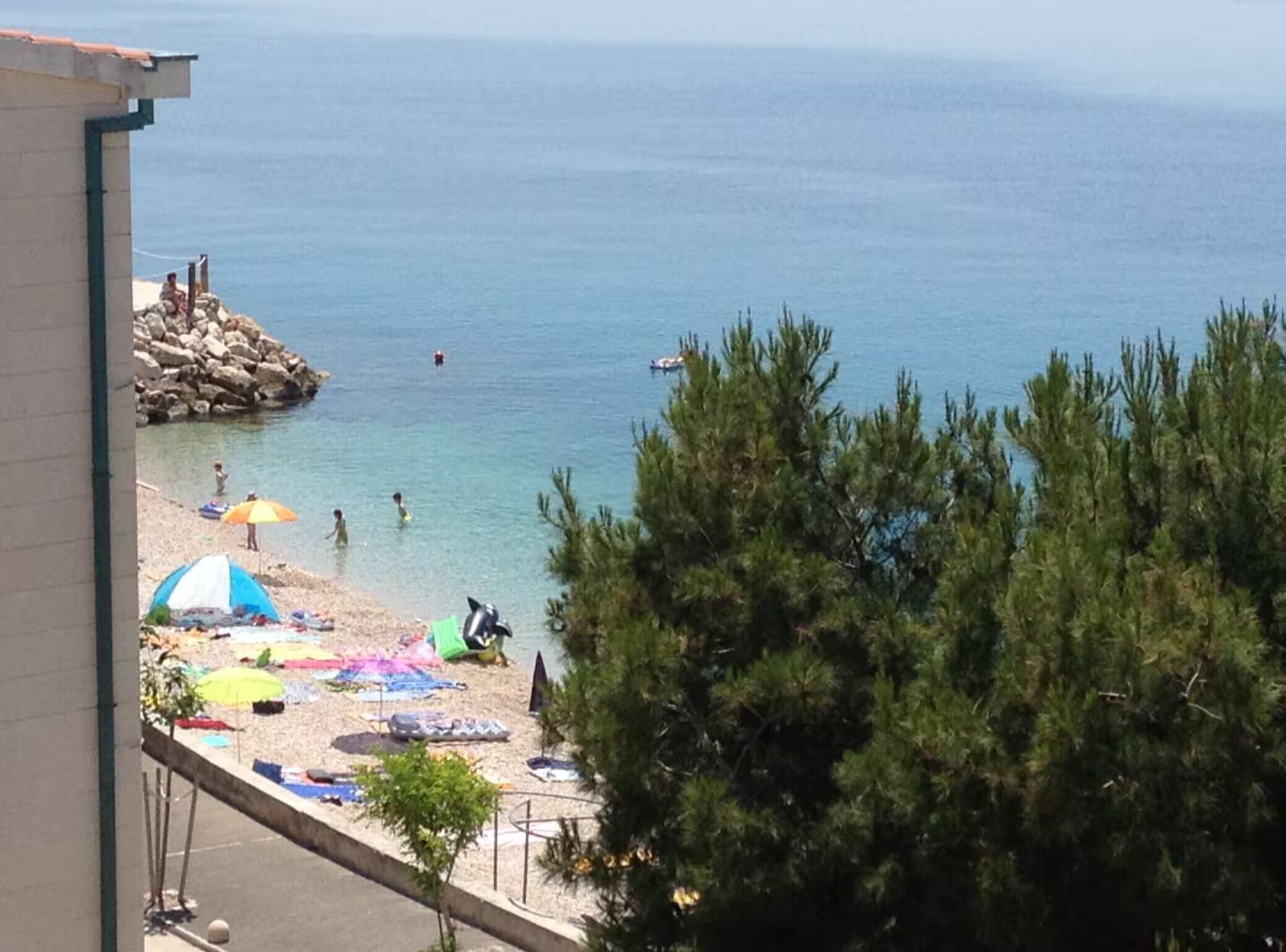 Ein Strand mit klarem Wasser, Sonnenschirmen und badenden Personen.
