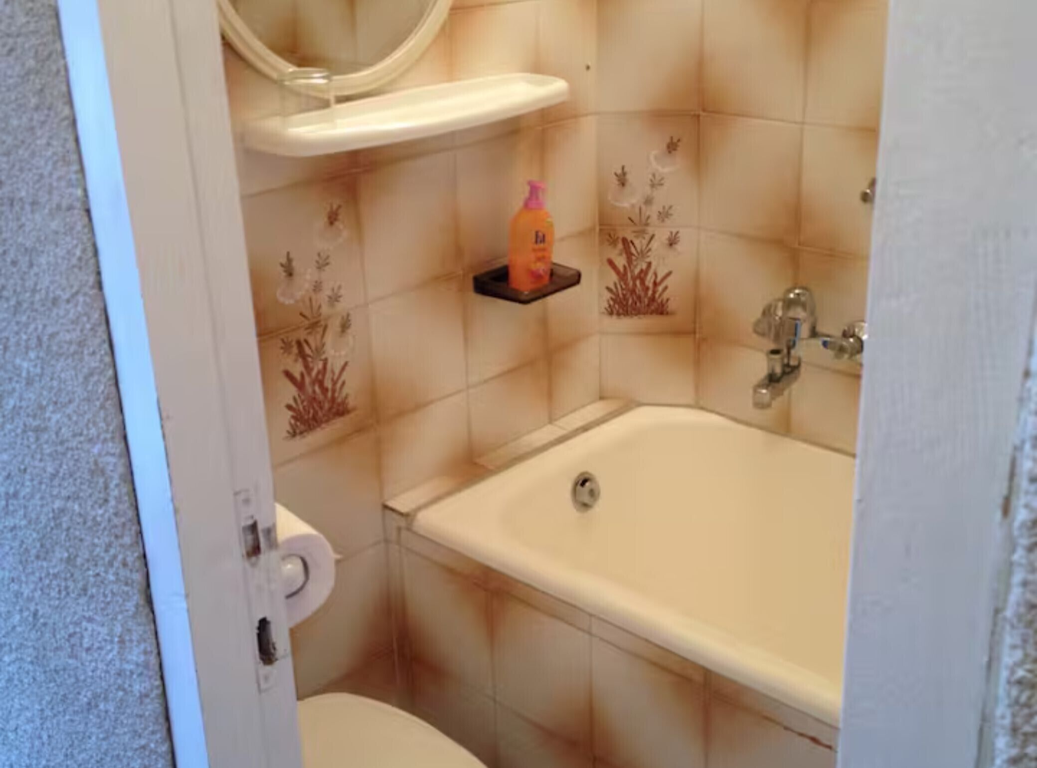 A bathroom with a bathtub, toilet, and a shelf with a bottle.