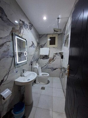 Un baño con pared de mármol, un lavabo, un inodoro, un espejo y una puerta.