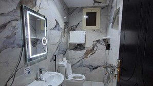 Un baño con pared de mármol, un lavamanos, un inodoro, un espejo y una puerta.