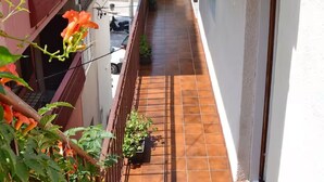 Een smal balkon met betegelde vloer, een metalen hekwerk en potplanten.