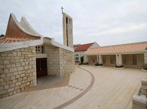 A courtyard with a church featuring a clock tower, stone walls, and a tiled roof. - Three Bedroom Apartment (Drasnice)
