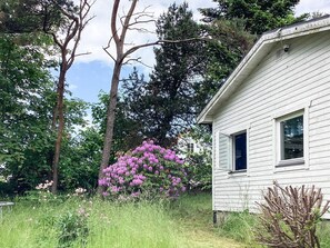 A white house with a window, surrounded by trees and purple flowers. - 5 Person Holiday Home in Bastad (Bastad)