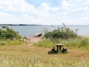 A lakeside picnic area with a wooden bench and table, a dock extending into the water, and a path leading to the dock. - 5 Person Holiday Home in Bastad (Bastad)