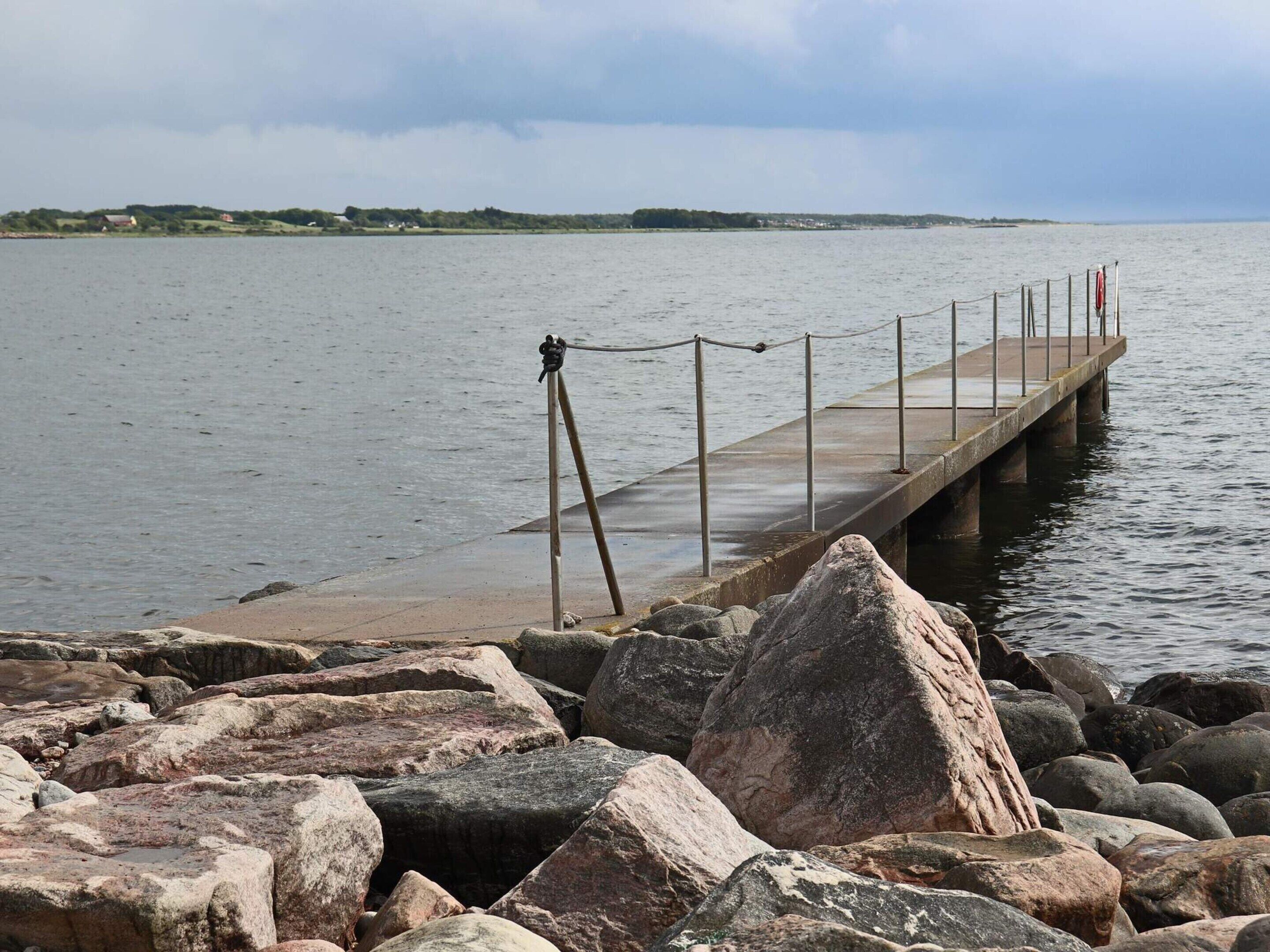 A pier extending into calm water, surrounded by large rocks.