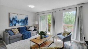 A modern living room with a grey sofa, a coffee table, and a painting on the wall. - Skyline Views, Sleeps 8 and only Steps to SAIT, U of C & Downtown! (Calgary)