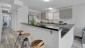 A modern kitchen with a central island, bar stools, and a view into the adjacent dining area. - Skyline Views, Sleeps 8 and only Steps to SAIT, U of C & Downtown! (Calgary)