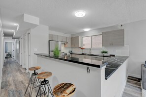 A modern kitchen with a central island, bar stools, and a view into the adjacent dining area.