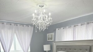 Ein Schlafzimmer mit Bett, einer Chandelier, Vorhängen, einer Nachttischlampe und einem Bild an der Wand.