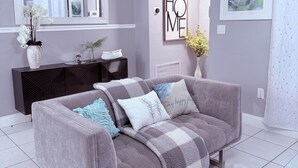 Ein modernes Wohnzimmer mit einem grauen Sofa, einem schwarzen Konsolentisch, einer weißen Vase mit Blumen, einem Schild mit der Aufschrift 'HOME' und einem Bild an der Wand.