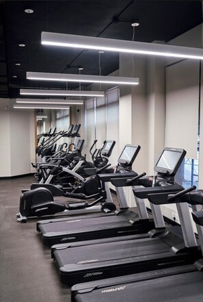 Un gimnasio con múltiples cintas de correr y elípticas, iluminación moderna y un diseño limpio y espacioso.