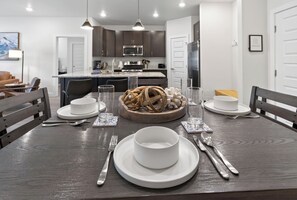 A dining area with a dark wooden table set for four, white plates, bowls, cutlery, and glasses. A woven basket centerpiece is on the table. - Brand new. Luxury Condo. Hot tub. Garage. (Keystone)
