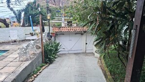 A paved pathway leading to a gated entrance with a tiled roof, surrounded by greenery and a stone wall. - Studio 81 (Rio de Janeiro)