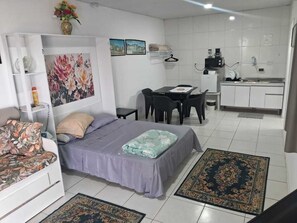 Ein kompakter Wohnbereich mit Bett, kleinem Tisch, Küchenzeile und Sitzecke.