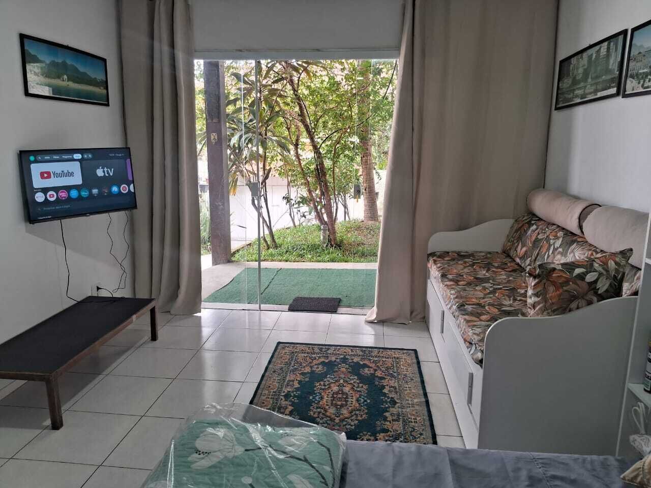 A living room with a sofa, a bench, a TV, and a view of a garden through a glass door.