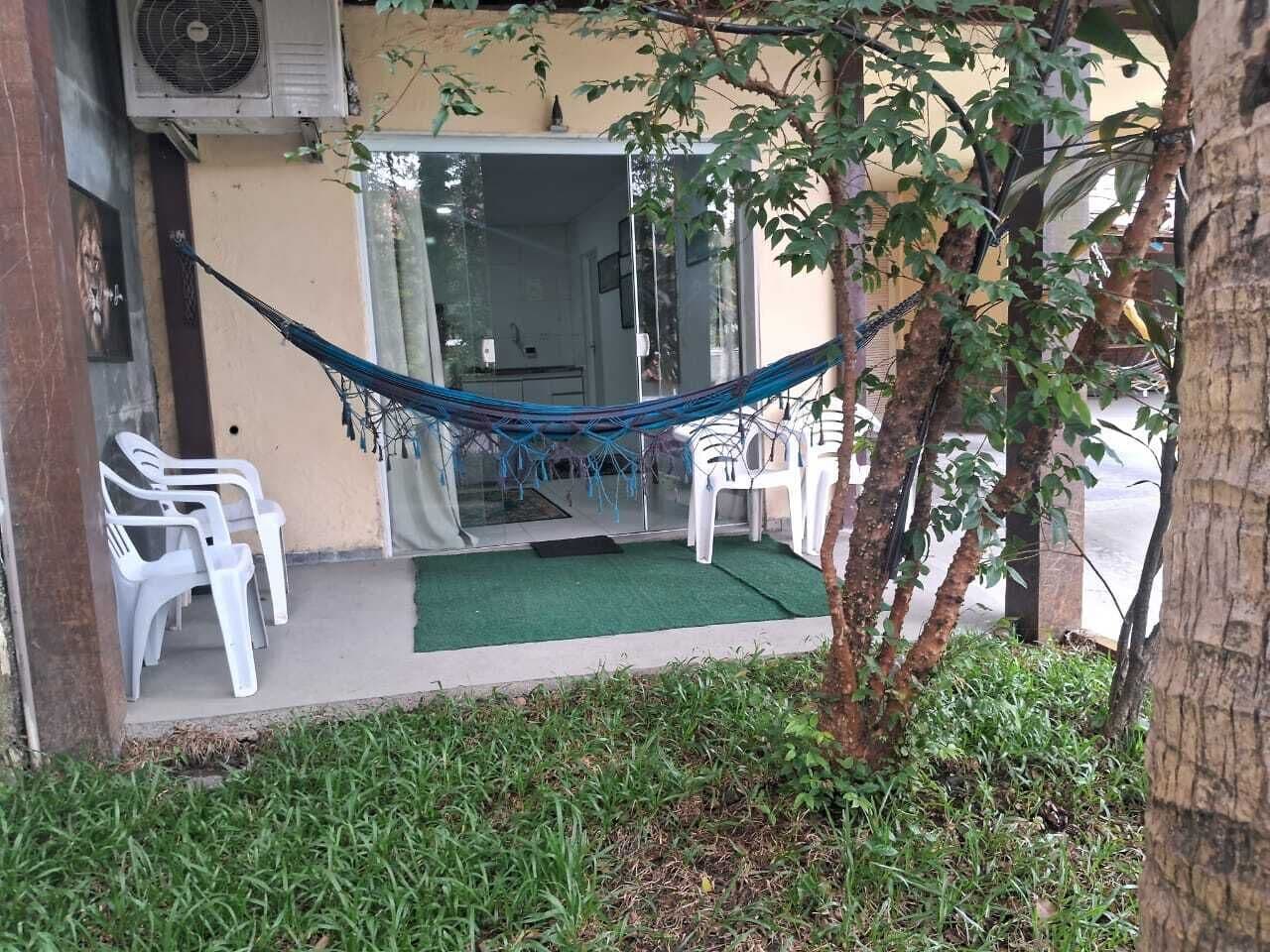 A hammock, white plastic chairs, and a small garden area with grass and a tree.
