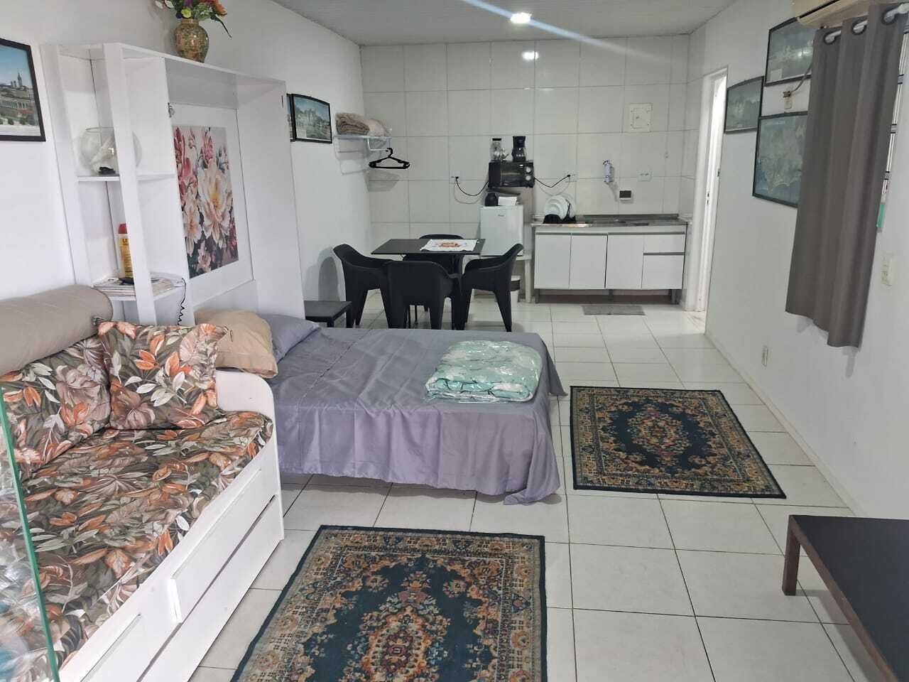 A compact living space with a sofa, a bed, a dining table with chairs, a kitchenette, and a bathroom.