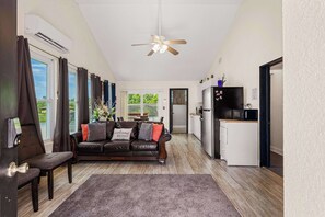 A living room with a sofa, a coffee table, a ceiling fan, and a kitchen area with a refrigerator and microwave. - Stylish Loft Retreat, Near Disney, Sleeps 6 (Kissimmee)