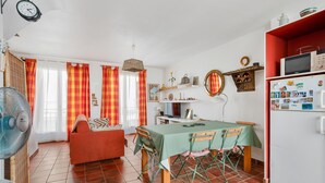 Ein Essbereich mit Tisch, Stühlen, einem Ventilator, einer Couch und einem Kühlschrank.