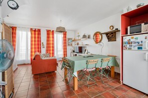 A dining area with a table, chairs, a fan, a sofa, and a refrigerator. - Patio Voltaire - A 5km de la plage (Sérignan)