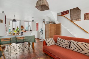 A living room with a sofa, a dining table, and a staircase with a wooden handrail. - Patio Voltaire - A 5km de la plage (Sérignan)