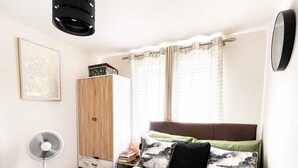 A bedroom with a bed, a bedside table, a wardrobe, a fan, and a window with curtains. - Welcome to Peace Pad 
Designed with comfort and convenience in mind. (Derby)