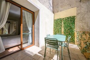 A room with a sliding glass door, a bed, a table with chairs, and a green leafy wall.