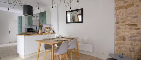 A modern kitchen with a central island, dining table, and chairs. There is a stone wall and a mirror on the wall.
