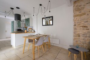 A modern kitchen with a central island, dining table, and chairs. There is a stone wall and a mirror on the wall.