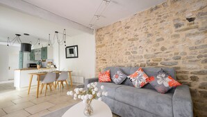 Ein modernes Wohnzimmer mit einem grauen Sofa, einem Essbereich mit Holztisch und einer Küche im Hintergrund.