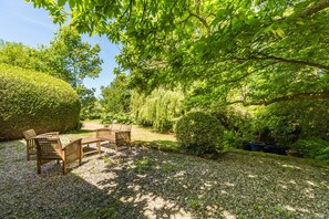 Ein Garten mit einem Holztisch und Stühlen, umgeben von viel Grün und einem Kiesweg.