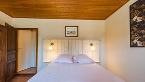 Un dormitorio con techo de madera, una cama con ropa de cama blanca, dos lámparas fijadas en la pared y un cuadro enmarcado sobre la cama.