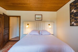 Ein Schlafzimmer mit Holzbalkendecke, einem Bett mit weißer Bettwäsche, zwei Wandleuchten und einem gerahmten Bild über dem Bett.