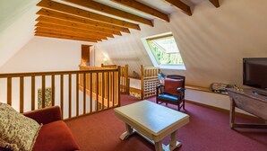 Una habitación acogedora en el ático con techo de madera, una pequeña mesa, una silla, un sofá, un televisor y una ventana.