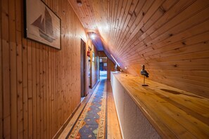Ein hölzerner Flur mit einem gemusterten Teppich, einem gerahmten Bild an der Wand und einer Leuchte rechts.