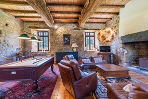 Ein gemütlicher Raum mit Billardtisch, Ledersofas, Kamin und Steinwänden.