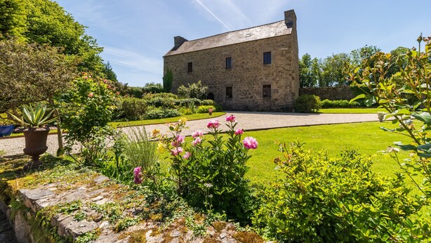 A stone building with a paved driveway and a well-maintained garden with various plants and flowers. - Le Manoir - Plouguiel (Plouguiel)